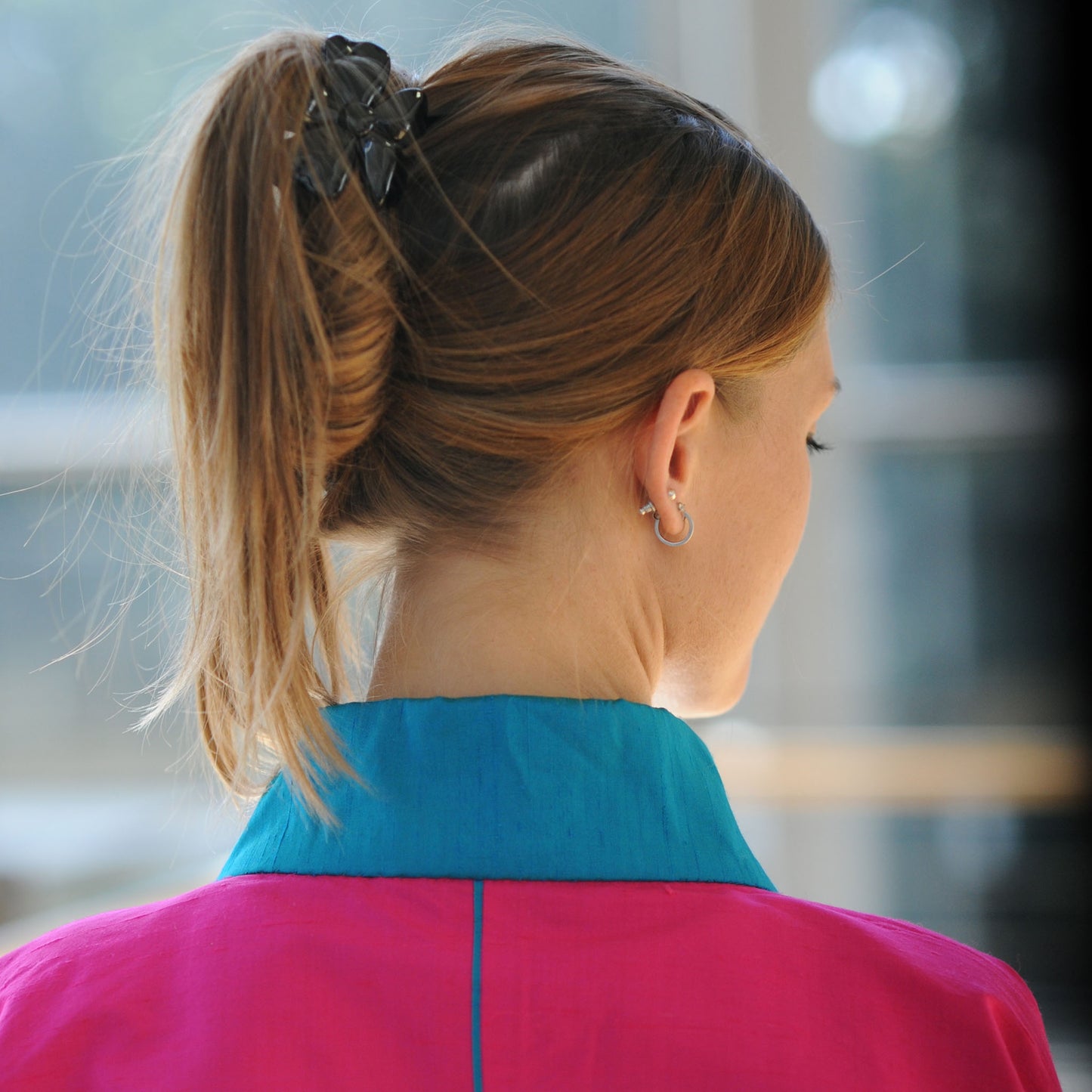 Eine junge Frau sieht nach rechts. Sie trägt einen Kimono von Design Gianni Sarto, mit blauem Kragen aus pinkfarbener Seide. Die hintere Mitte ist durch eine blaue Paspel betont.