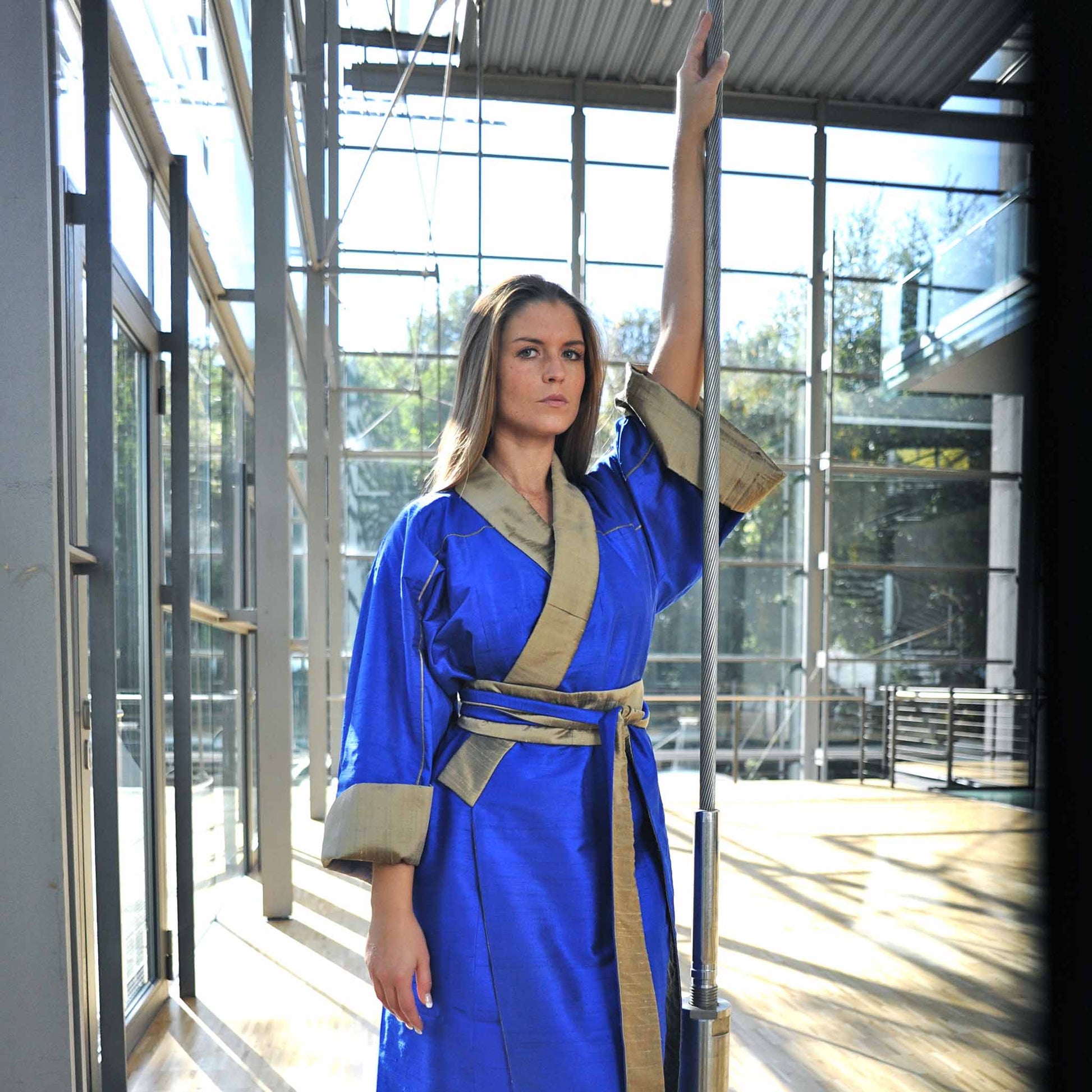 Eine junge Fraugeht steht frontal zur Kamera. Sie trägt einen SeidenKimono von Design Gianni Sarto, mit den Farben Blau und gold..